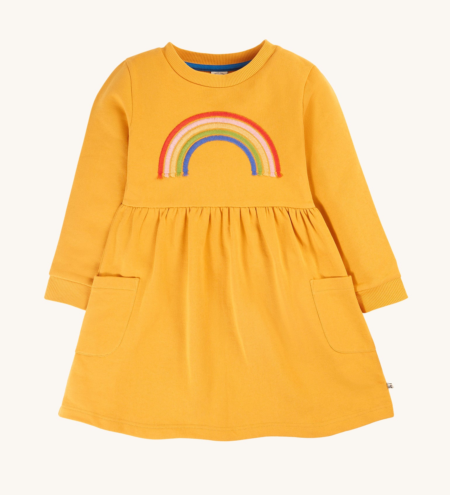 This beautiful long sleeve Niamh Dress from Frugi features a soft gathered waist and patch pockets. Made from super soft and durable organic cotton in Gold with a Rainbow embroidery detail on the front.