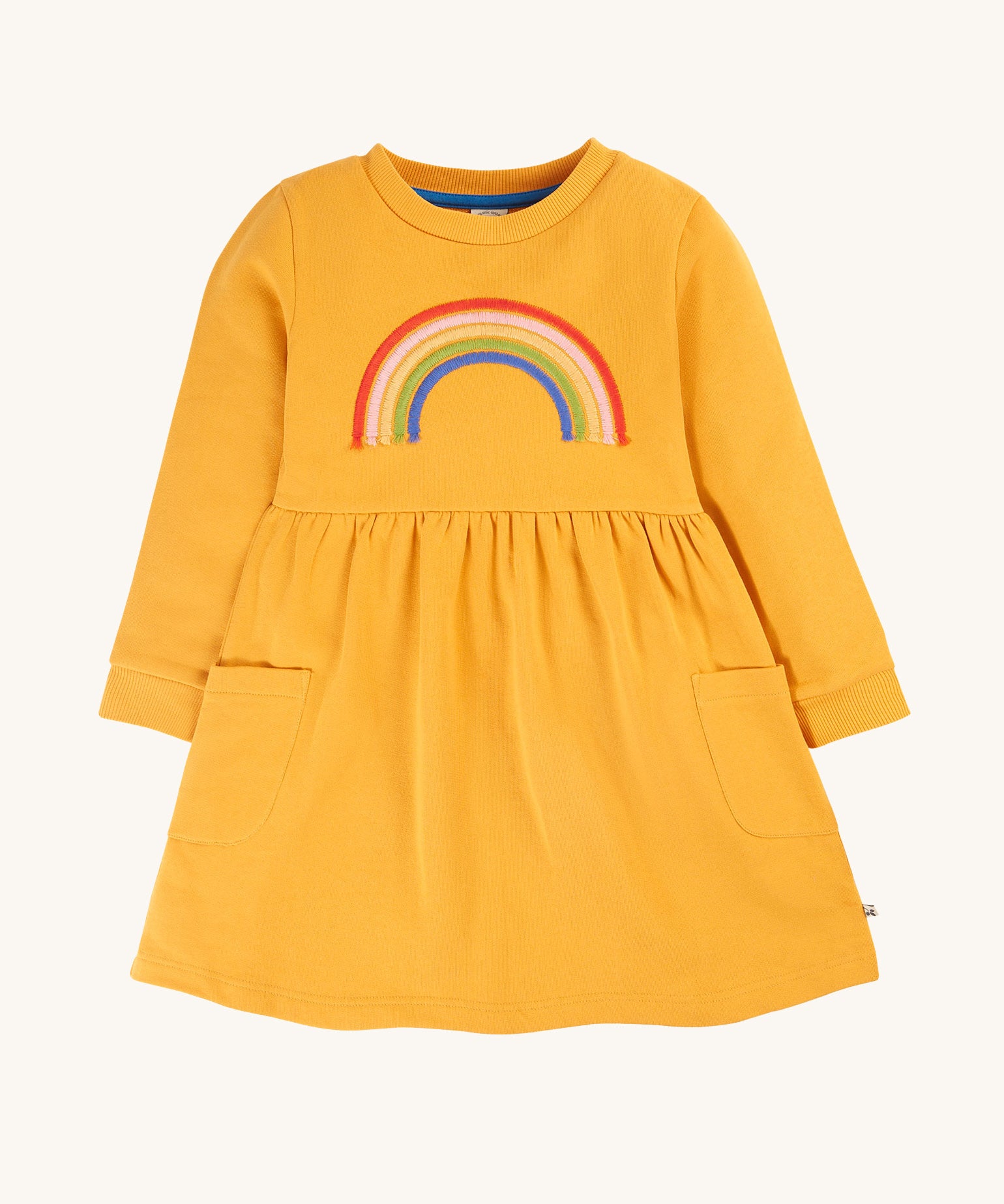 This beautiful long sleeve Niamh Dress from Frugi features a soft gathered waist and patch pockets. Made from super soft and durable organic cotton in Gold with a Rainbow embroidery detail on the front.