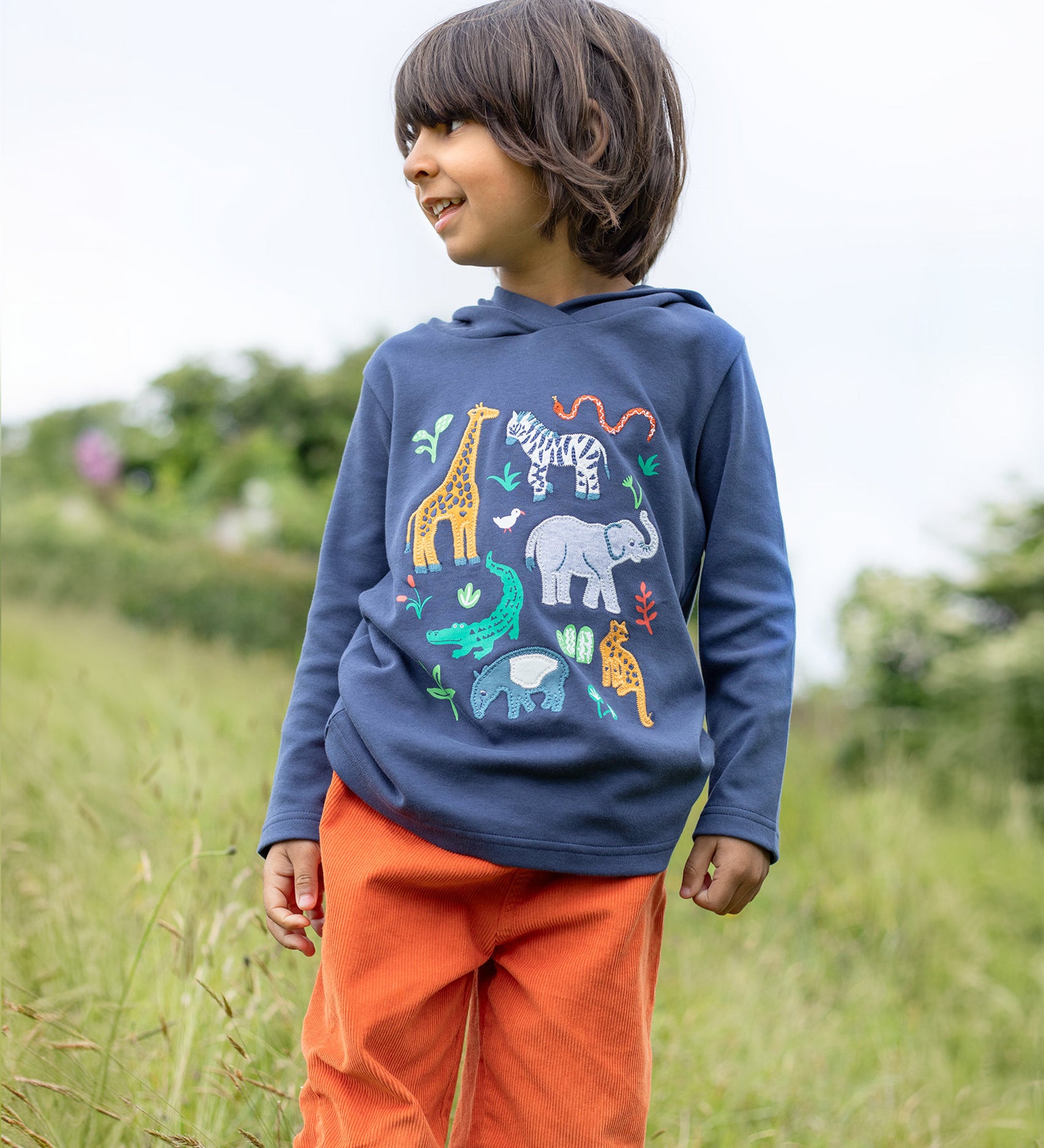 A child outside, wearing the Frugi Campfire Hooded Top - Navy Blue/Go Wild Animals and orange Frugi cord trousers