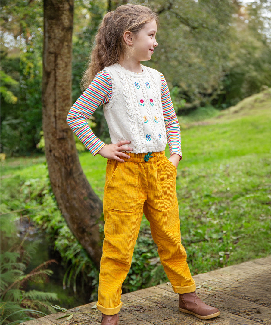 A child wearing the Frugi Marnie Embroidered Tank Top - Pearl/Flowers, and yellow cord Frugi trousers