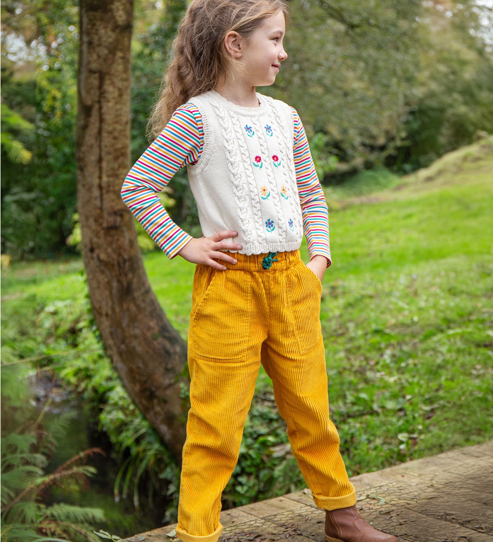 A child wearing the Frugi Marnie Embroidered Tank Top - Pearl/Flowers, and yellow cord Frugi trousers