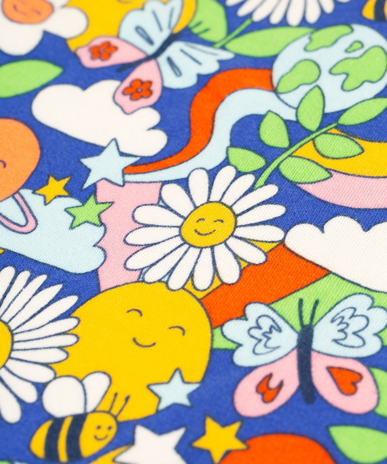 A closer look at the Frugi Retro Happy print. The image shows colourful smiling flowers and planets, stars, clouds, a bee and a butterfly on a royal blue fabric