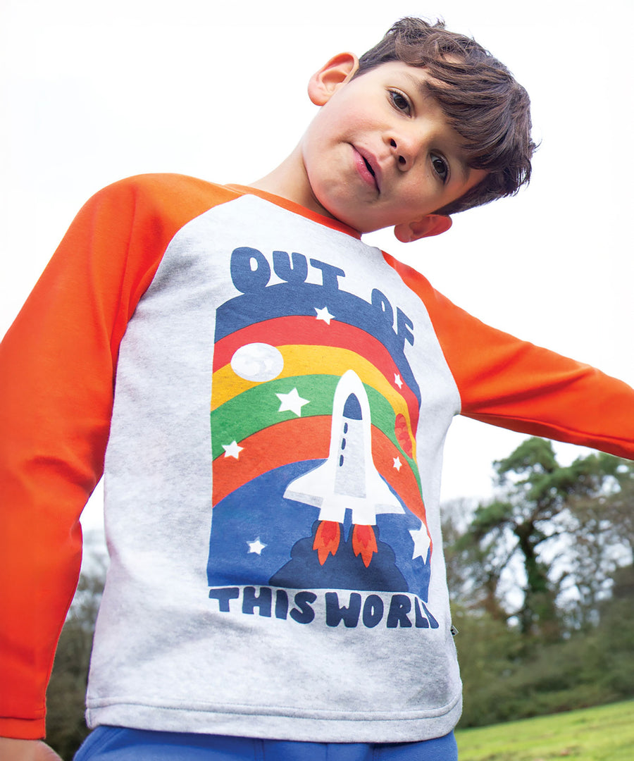 A child stood outside, wearing the Frugi Tamar Raglan Top - Grey Marl/Out Of This World