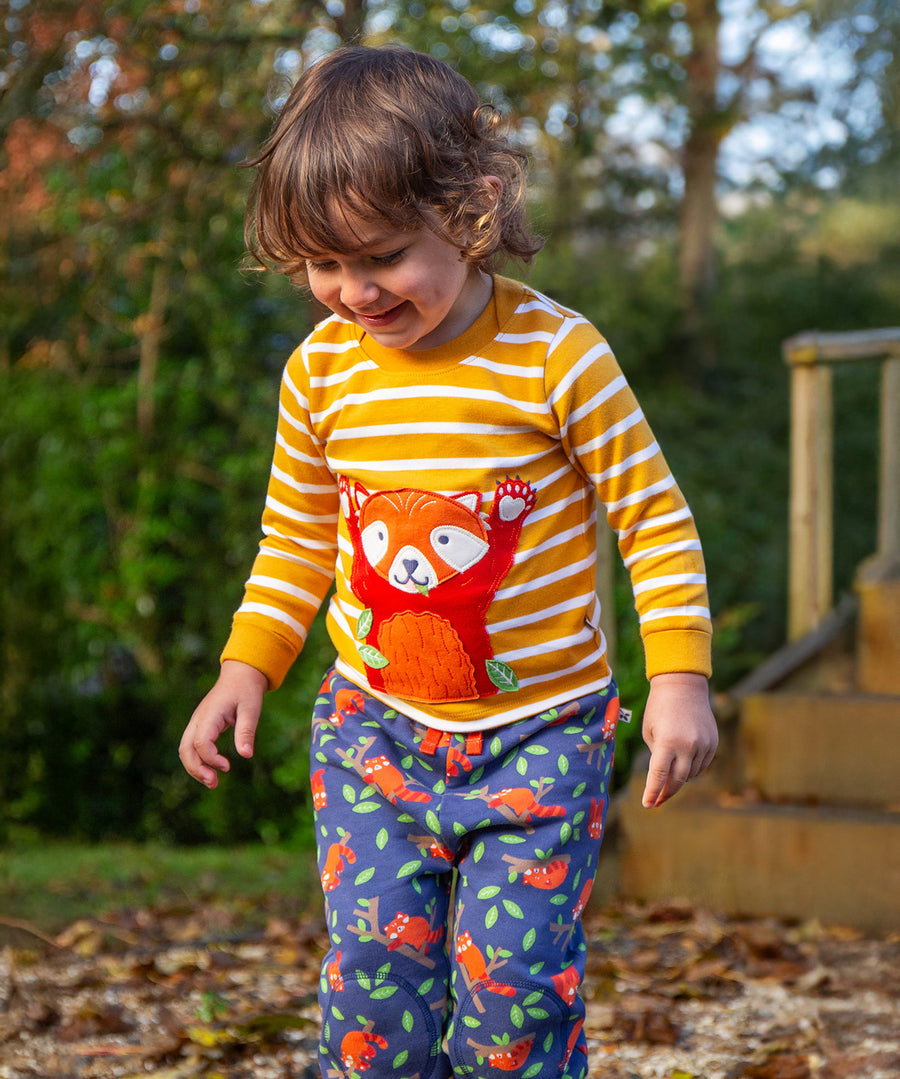 A child playing outside in the autumn leaves, wearing the Frugi Snuggle Crawlers - Red Panda Pals