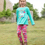 A child outside wearing the Frugi Anna Applique Top - Pacific Aqua/Horse, and Frugi Wild Horses leggings