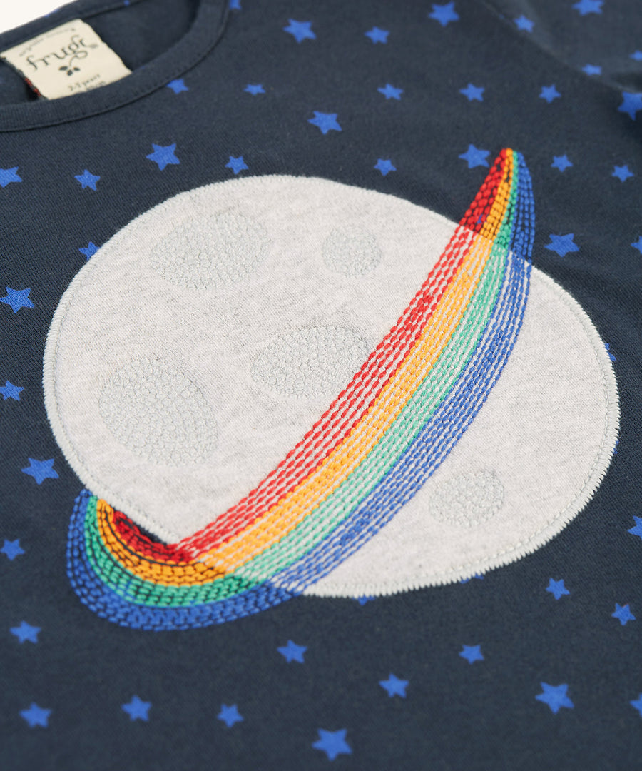 A closer look at the planet applique on the Frugi Tully Applique Top - Starry Night/Planet. The images shows embroidered detailing on the plant which looks like moon craters, and rainbow embroidered rings around the planet