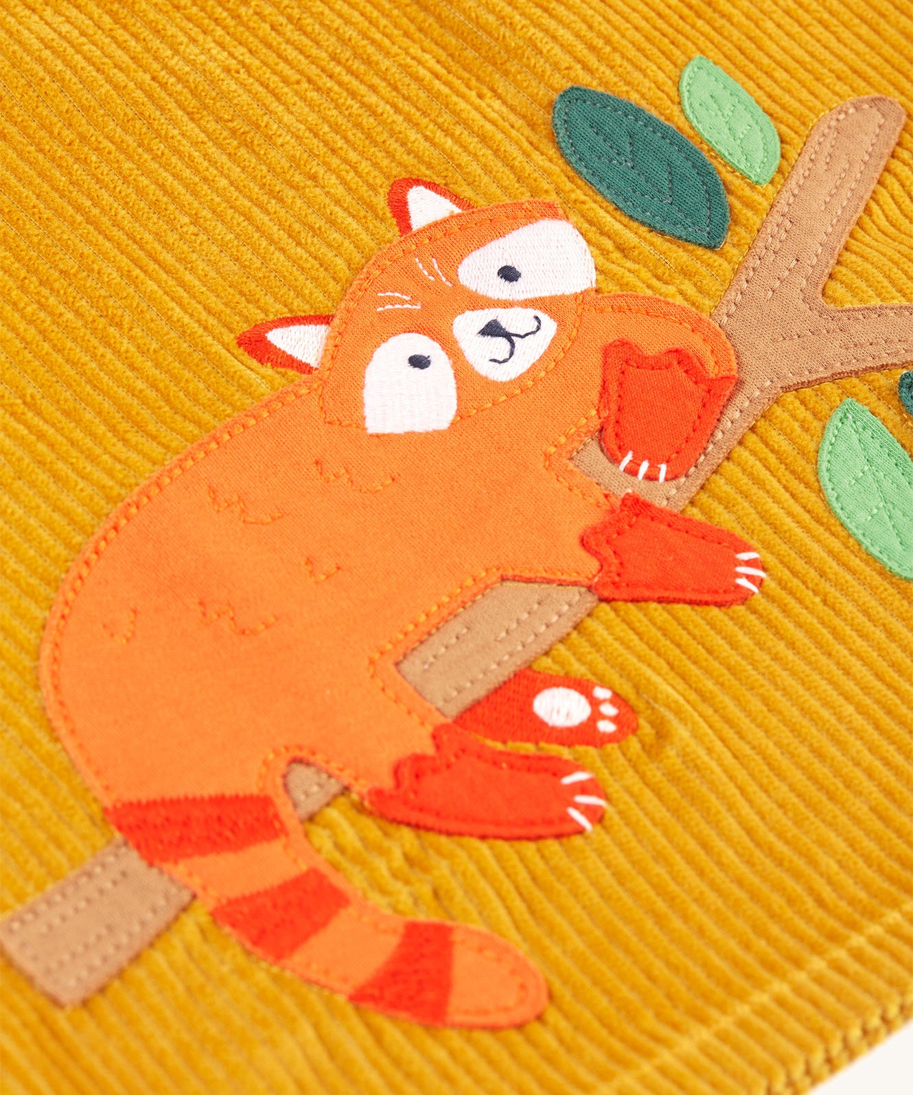 A closer look at the Red Panda on a tree branch applique. The Panda has a smiling face, an orange body and tail, with red ear tips, red tail stripes and red paws. The branch is light brown and the leaves are light and dark green.