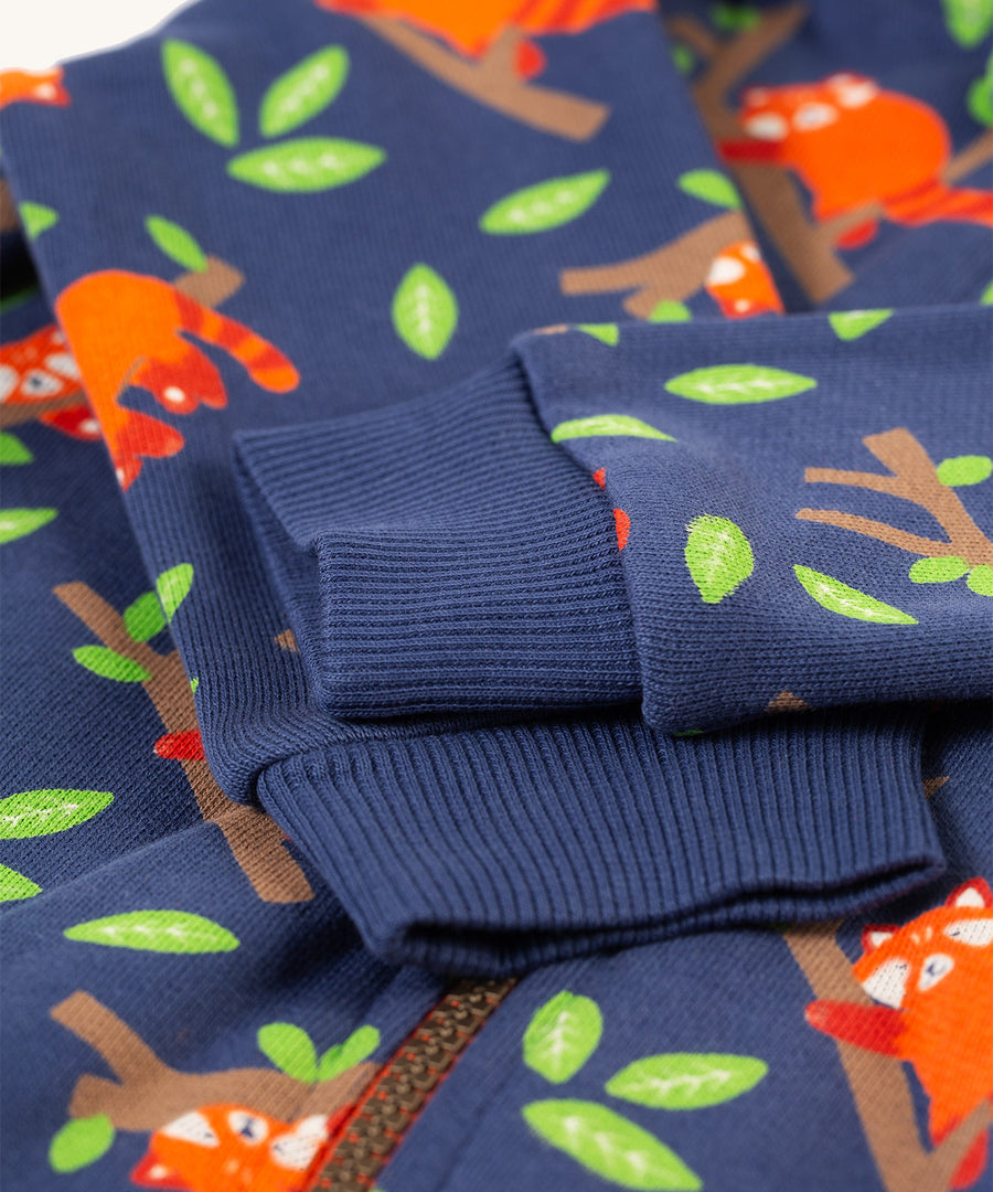 A closer look at the blue, elasticated rubbed cuffs on the Frugi Snuggle Suit - Red Panda Pals. The image also shows the red pandas, leaves and branch patterns, along with part of the snuggle suit zip