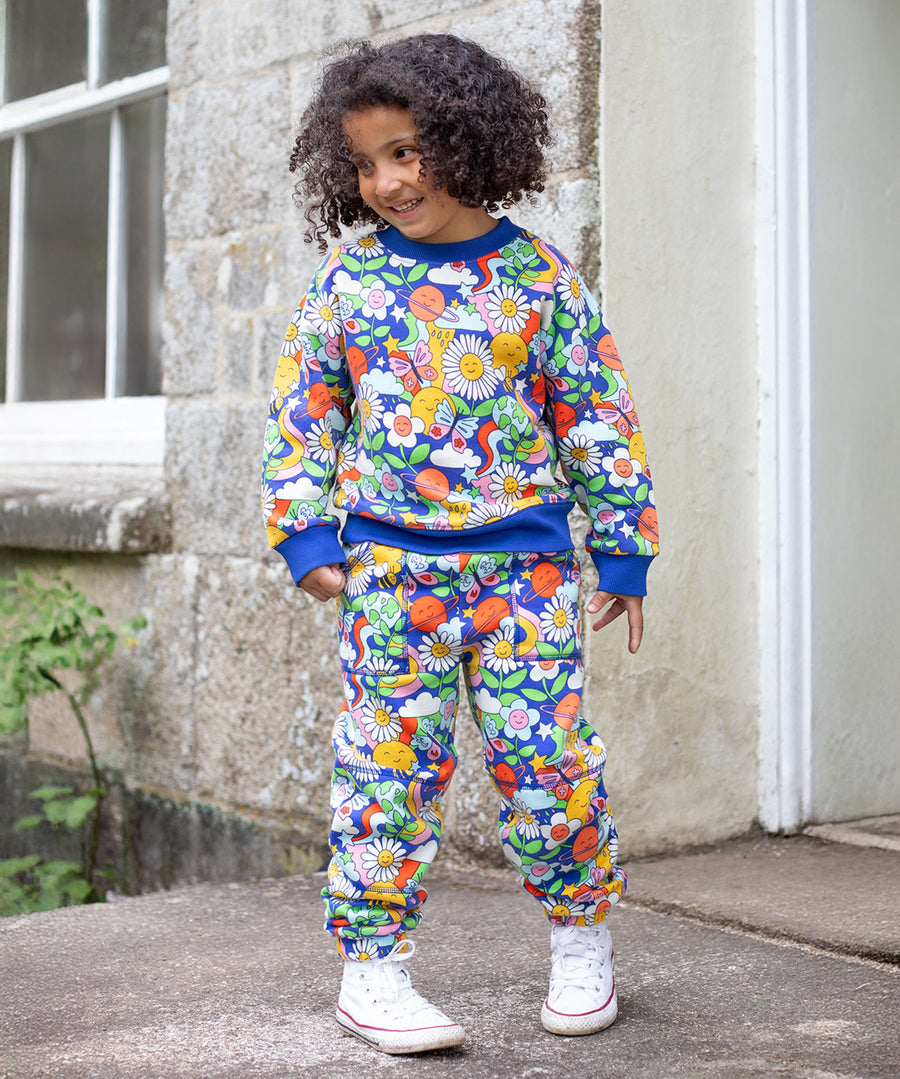 A child stood outside of a house, wearing the Frugi Malpas Joggers - Retro Happy, and the Frugi Retro Happy Sweatshirt