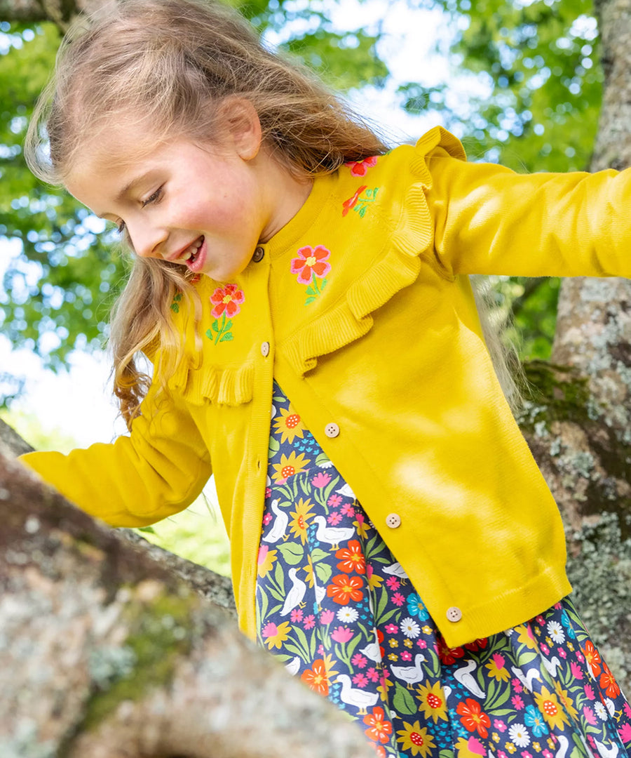 A child outside climbing a tree, wearing the Frugi Romi Ruffle Cardigan - Dandelion/Flowers