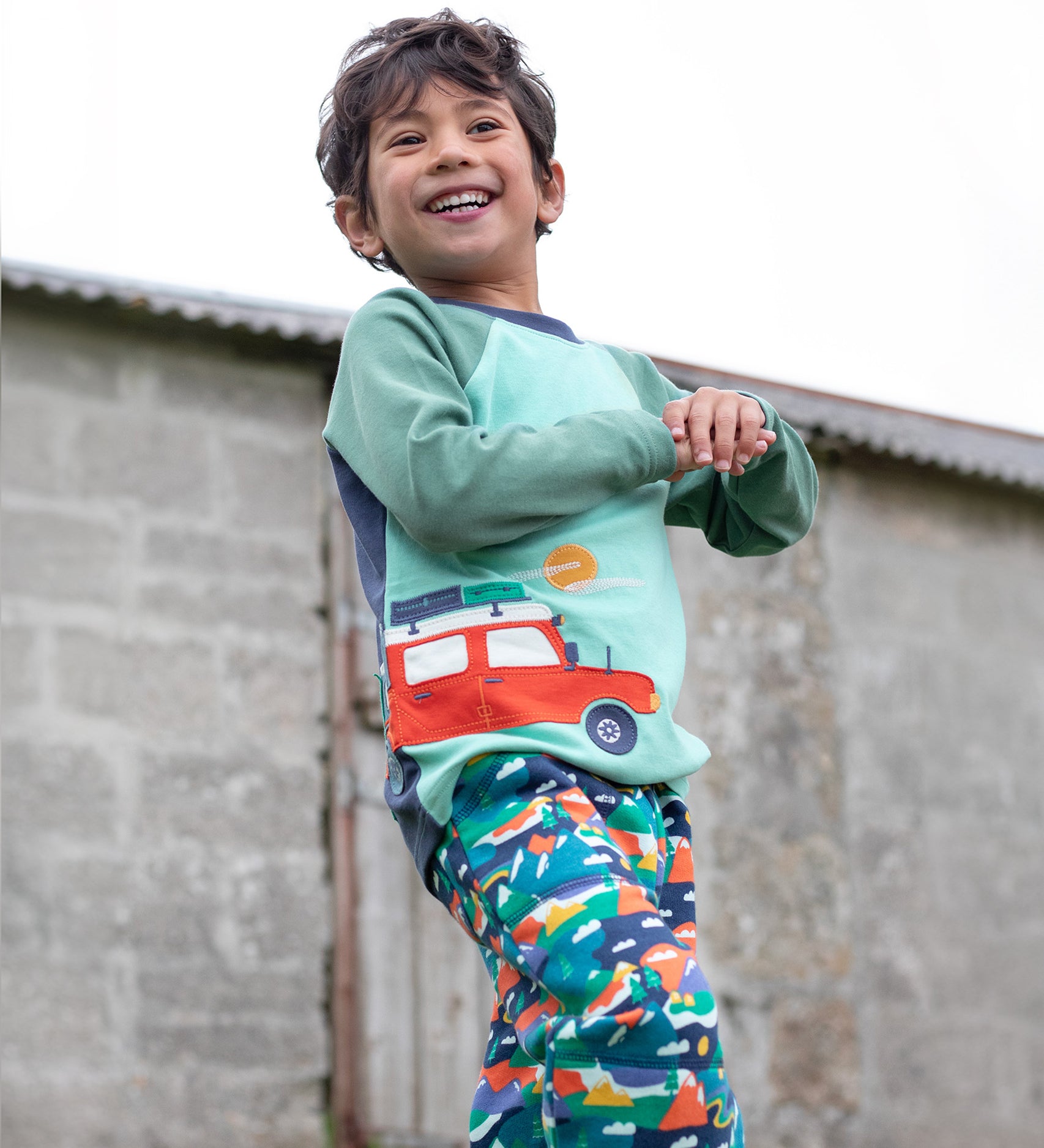 A child wearing the Frugi Albert Wrap Around Top - Moss/4X4 Camper, and Frugi Alpine trousers