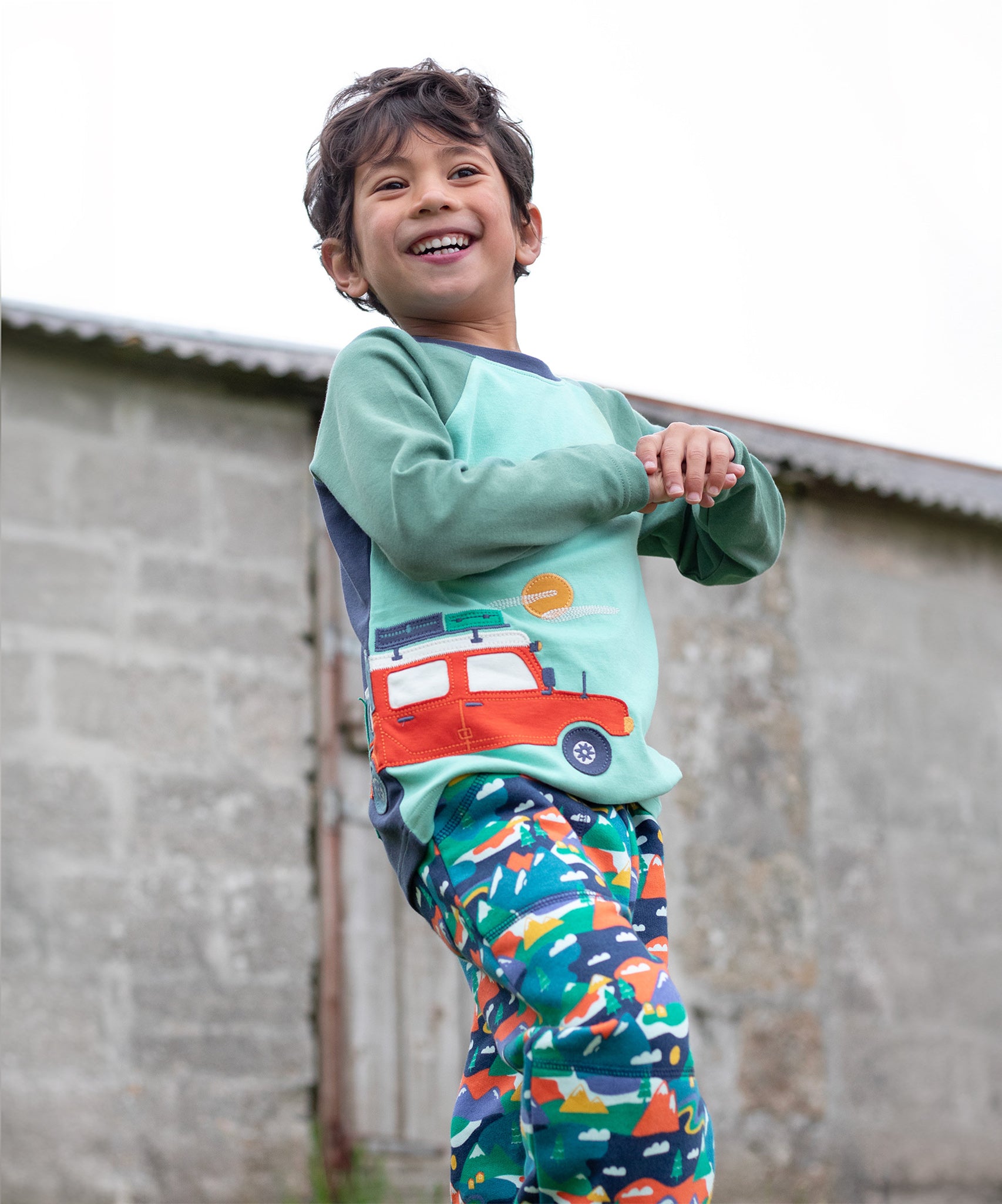 A child wearing the Frugi Albert Wrap Around Top - Moss/4X4 Camper, and Frugi Alpine trousers