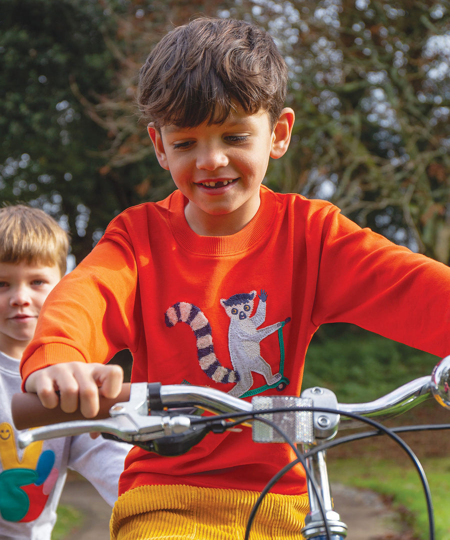 A child riding a bike whilst wearing the Frugi Owen Top - Bonfire/Lemur