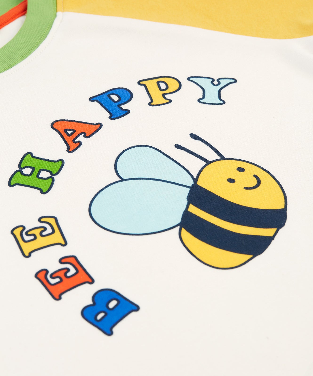 The Bee and Bee Happy logo on the Frugi Tamar Raglan Top - Soft White/Bee Happy