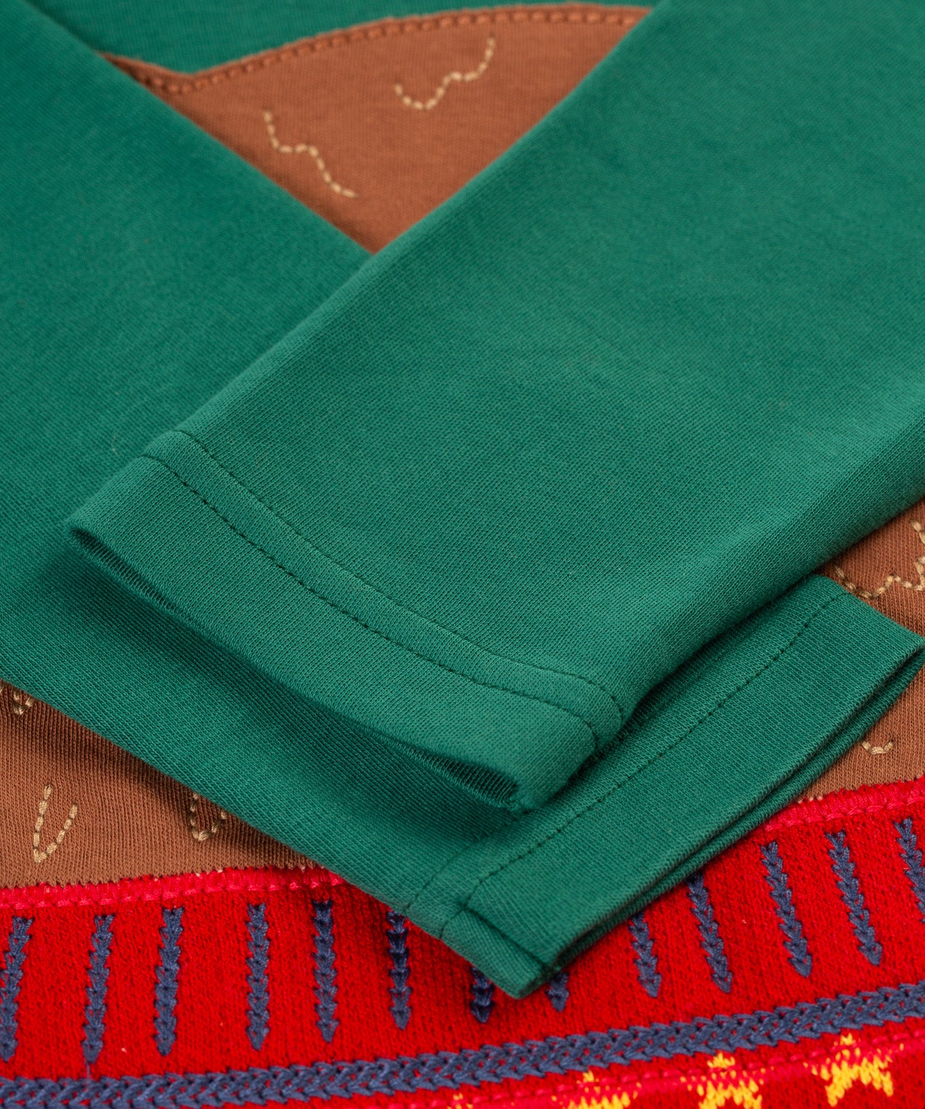 A closer look at the green sleeves on the Frugi Terrific Applique Top - Teal/Fairisle Bear. The bear applique is partially shown behind the folded sleeves