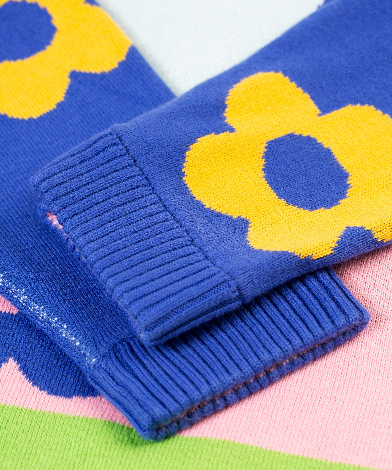 A closer look at the ribbed, knitted cuffs on the Frugi Zola Reversible Knitted Dress - Blue Tang/Retro Floral. The image shows royal blue sleeves with bold, yellow floral prints