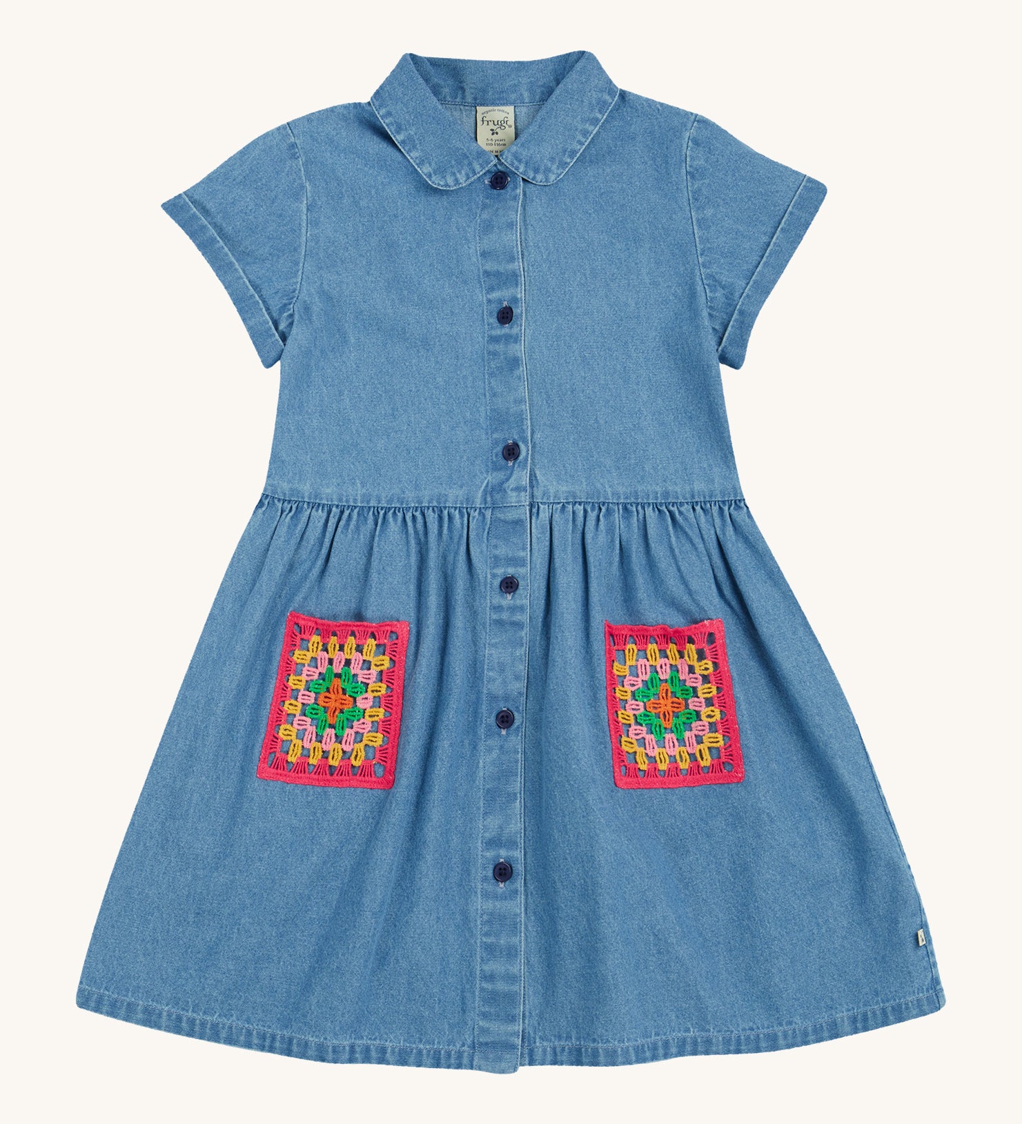 Frugi blue denim dress crochet pocket design on a cream background.