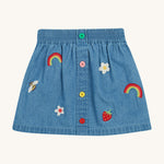 Frugi kids denim skirt with a flower, rainbow and strawberry design on a cream background.