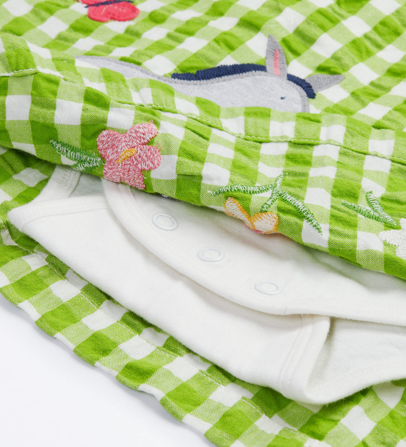 Close up of the Frugi little kids green gingham, donkey myrtle body dress - showing a grey donkey appliqué and a white underneath body garment underneath on green and white gingham organic cotton fabric