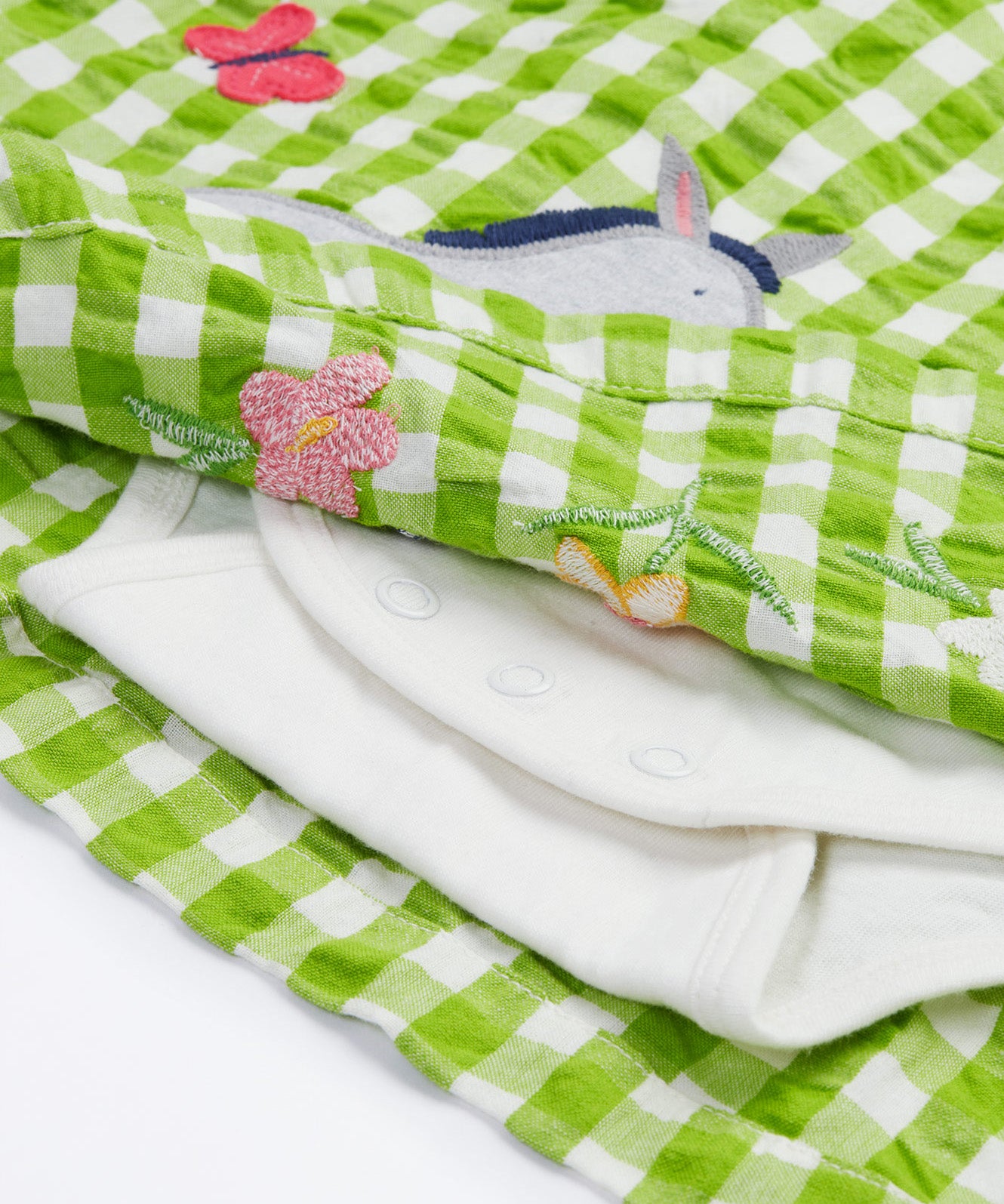 Close up of the Frugi little kids green gingham, donkey myrtle body dress - showing a grey donkey appliqué and a white underneath body garment underneath on green and white gingham organic cotton fabric