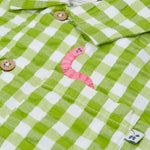 Close up of the Frugi Reggie kids shirt. showing the worm embroidery on the front pocket on green gingham organic cotton fabric