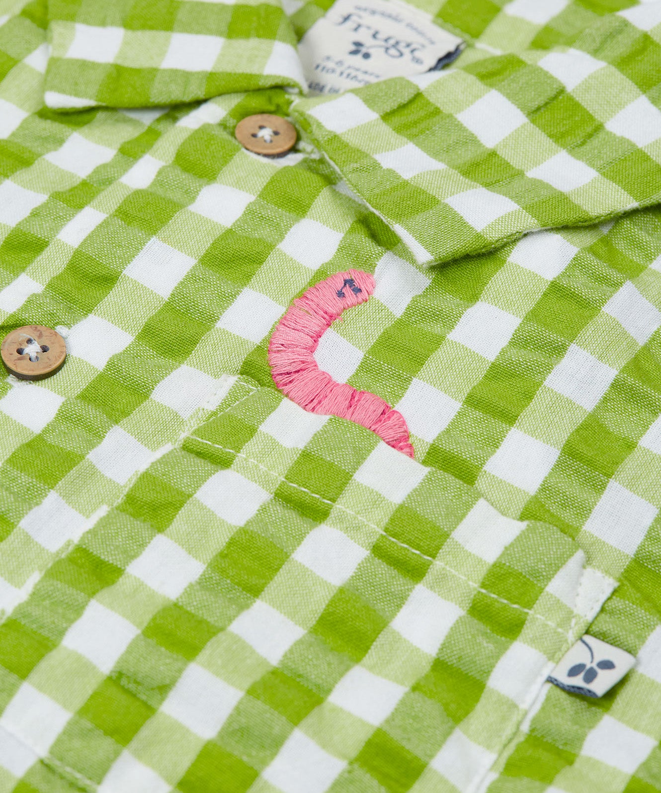 Close up of the Frugi Reggie kids shirt. showing the worm embroidery on the front pocket on green gingham organic cotton fabric