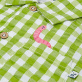 Close up of the Frugi Reggie kids shirt. showing the worm embroidery on the front pocket on green gingham organic cotton fabric