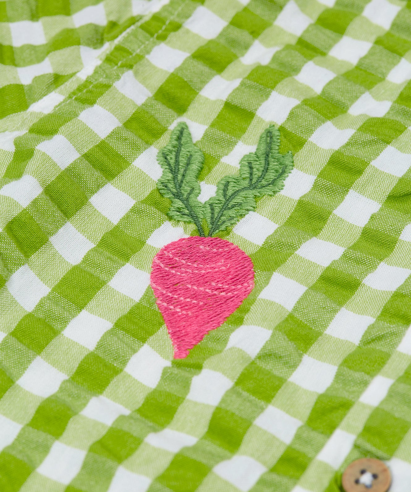 Close up of the Frugi Reggie kids shirt. showing the beetroot embroidery detail on green gingham organic cotton fabric