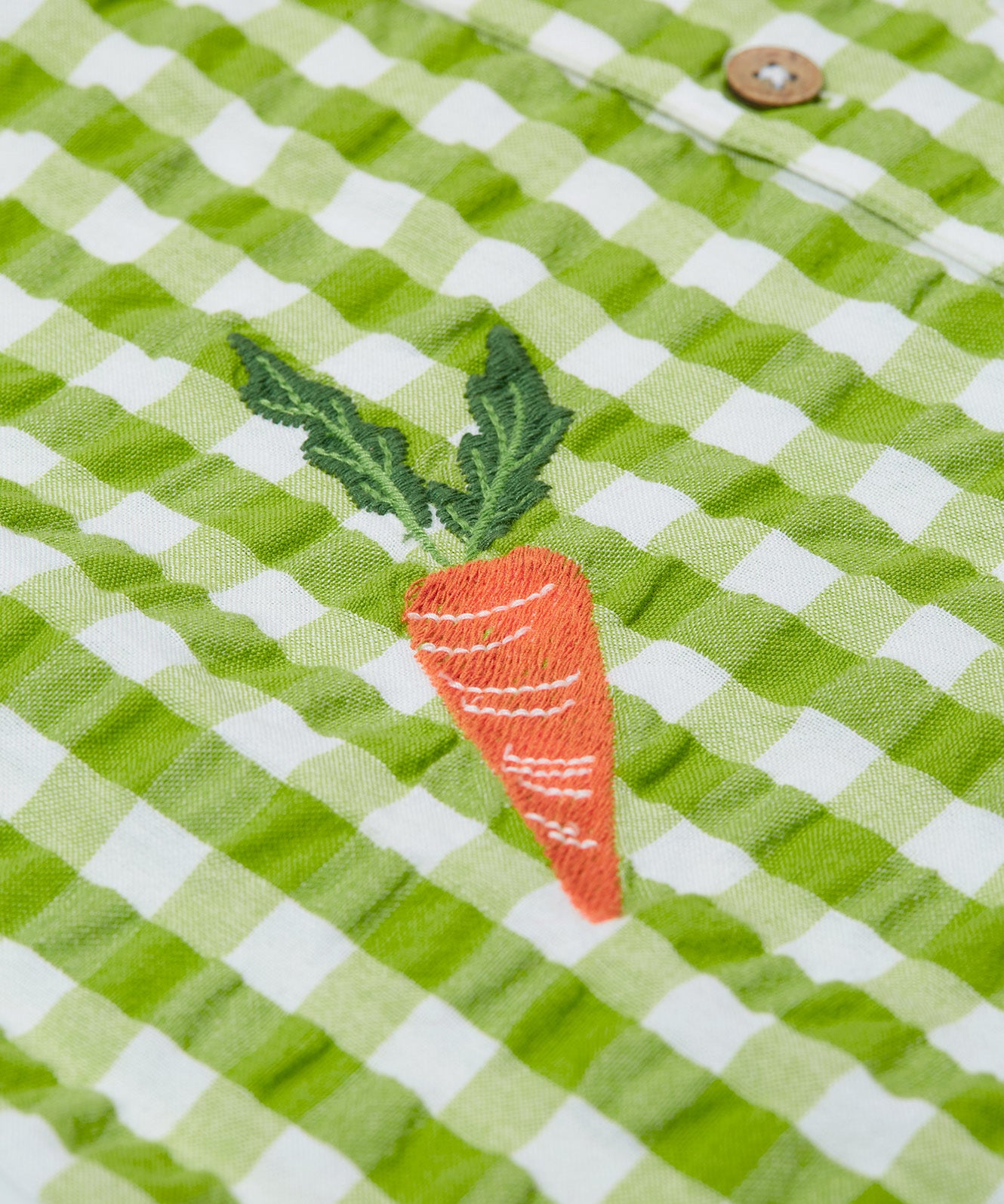 Close up of the Frugi Reggie kids shirt. showing the carrot embroidery on  green gingham organic cotton fabric