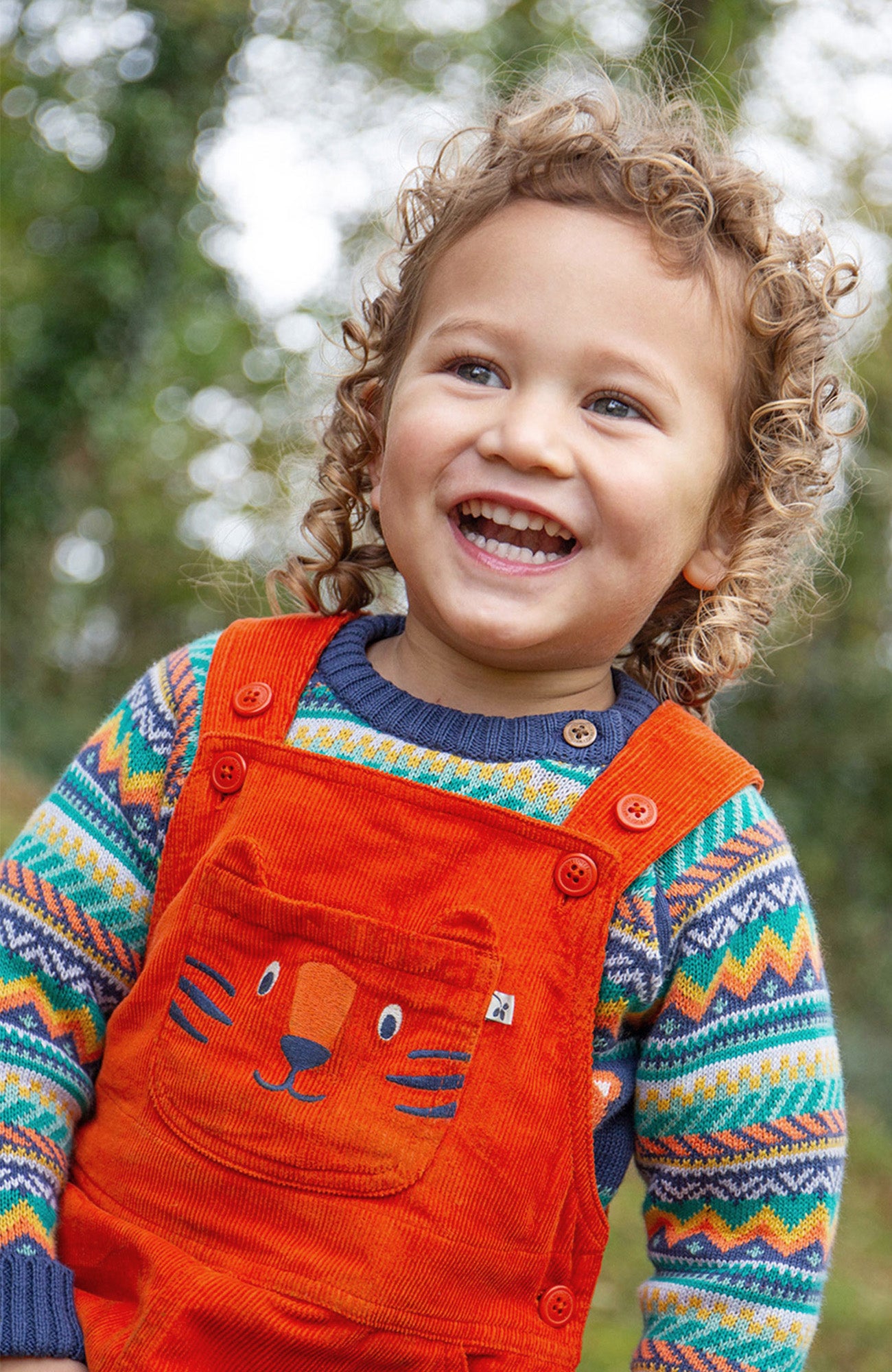 Child next to tree outdoors wearing cream frugi fleece with flower print