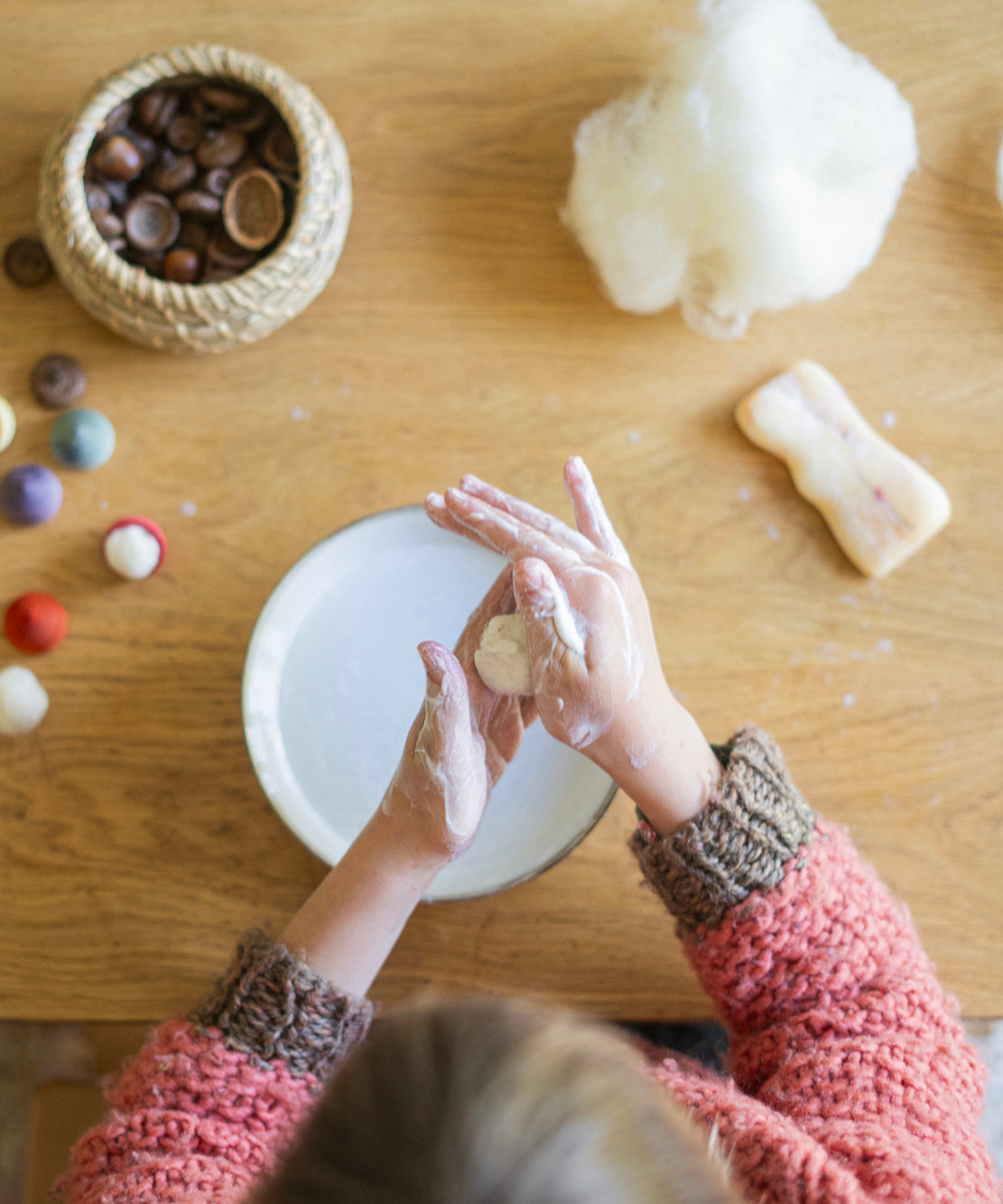 A child is creating a woolen ball craft using pieces from the Grapat Advent Calendar 2024. The little wool ball looks like a small snow ball