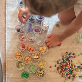 Child playing with the Grapat Mis Match & Bloom set, featuring colourful geometric pieces and sorting pots on a rug.