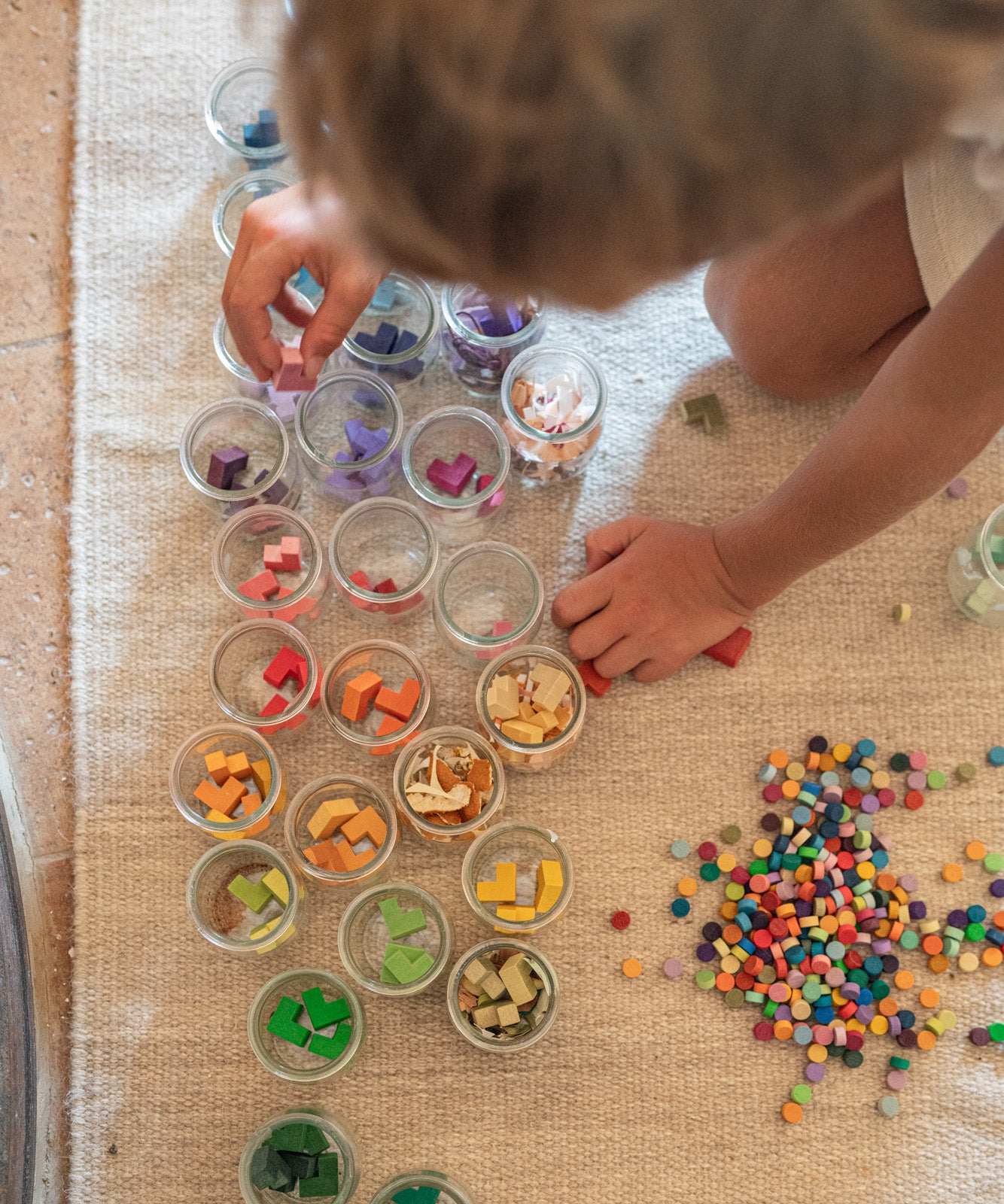 Child playing with the Grapat Mis Match & Bloom set, featuring colourful geometric pieces and sorting pots on a rug.