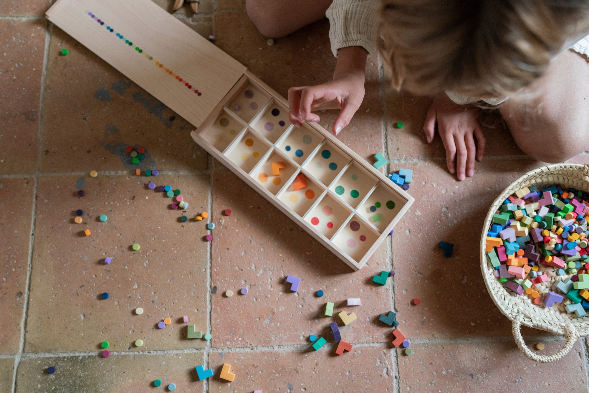 A child sorting the Grapat wooden bloom mis and match block set into a wooden sorting box on the floor 