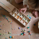 A child sorting the Grapat wooden bloom mis and match block set into a wooden sorting box on the floor 