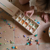 A child sorting the Grapat wooden bloom mis and match block set into a wooden sorting box on the floor 