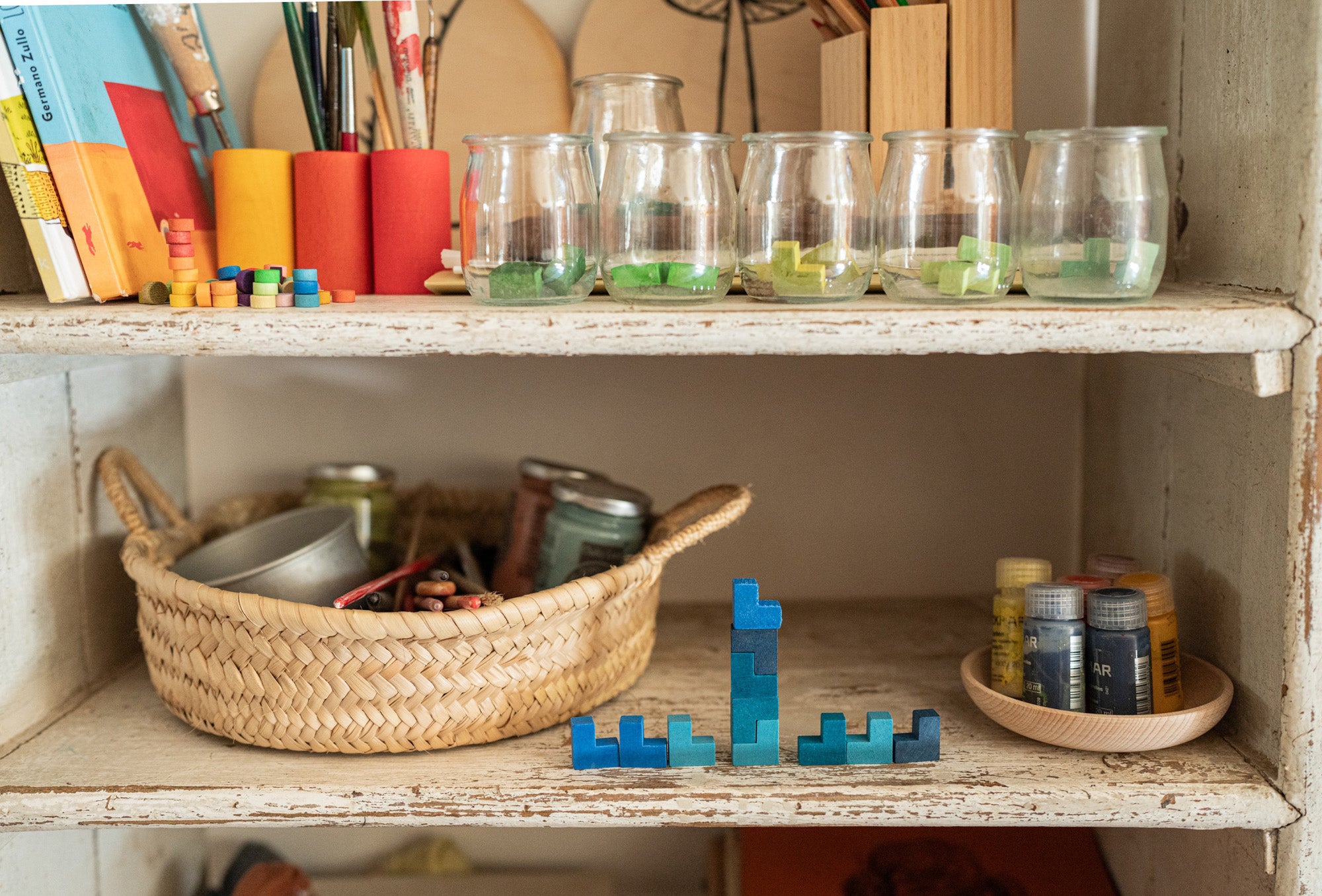 A close up of the Grapat mis match bloom set showing the blue wooden geometric pieces stacked on top of each other on a shelf with additional pieces in jars on another shelf