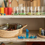 A close up of the Grapat mis match bloom set showing the blue wooden geometric pieces stacked on top of each other on a shelf with additional pieces in jars on another shelf