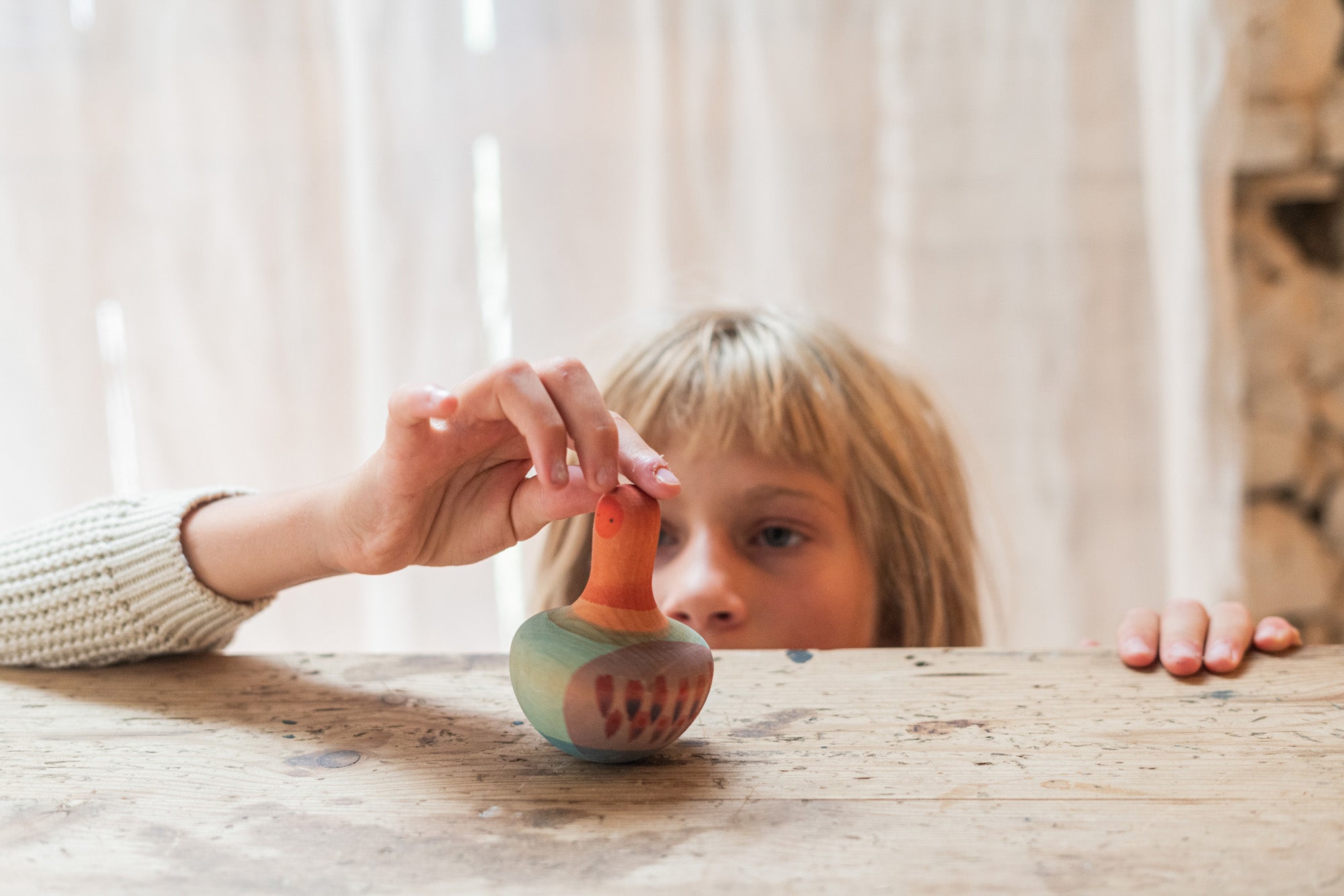 A child playing with the Grapat wooden mellow orange bird on a wooden table