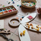 A child playing with the Grapat wooden bloom mis and match wooden block set. Featuring wooden Grapat petals a wooden fork and braided yarn and a woven basket on a terracotta floor