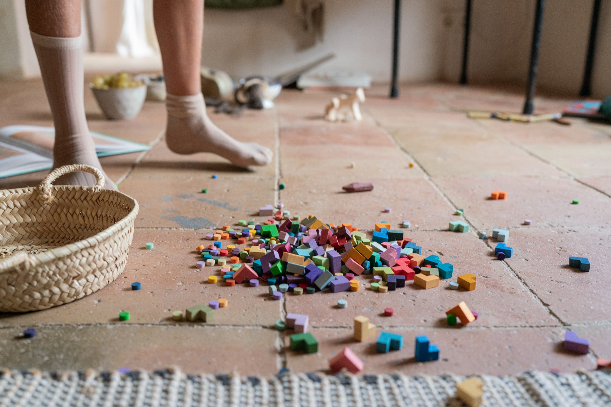 A close up of the Grapat mis match bloom set. Showing the different coloured geometric pieces on a terracotta floor next to a woven basket and child's legs. 