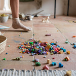 A close up of the Grapat mis match bloom set. Showing the different coloured geometric pieces on a terracotta floor next to a woven basket and child's legs. 