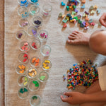 Child playing with the Grapat Mis Match & Bloom set featuring colourful geometric pieces, sorting jars with scattered colourful geometric pieces.