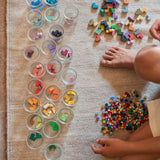 Child playing with the Grapat Mis Match & Bloom set featuring colourful geometric pieces, sorting jars with scattered colourful geometric pieces.