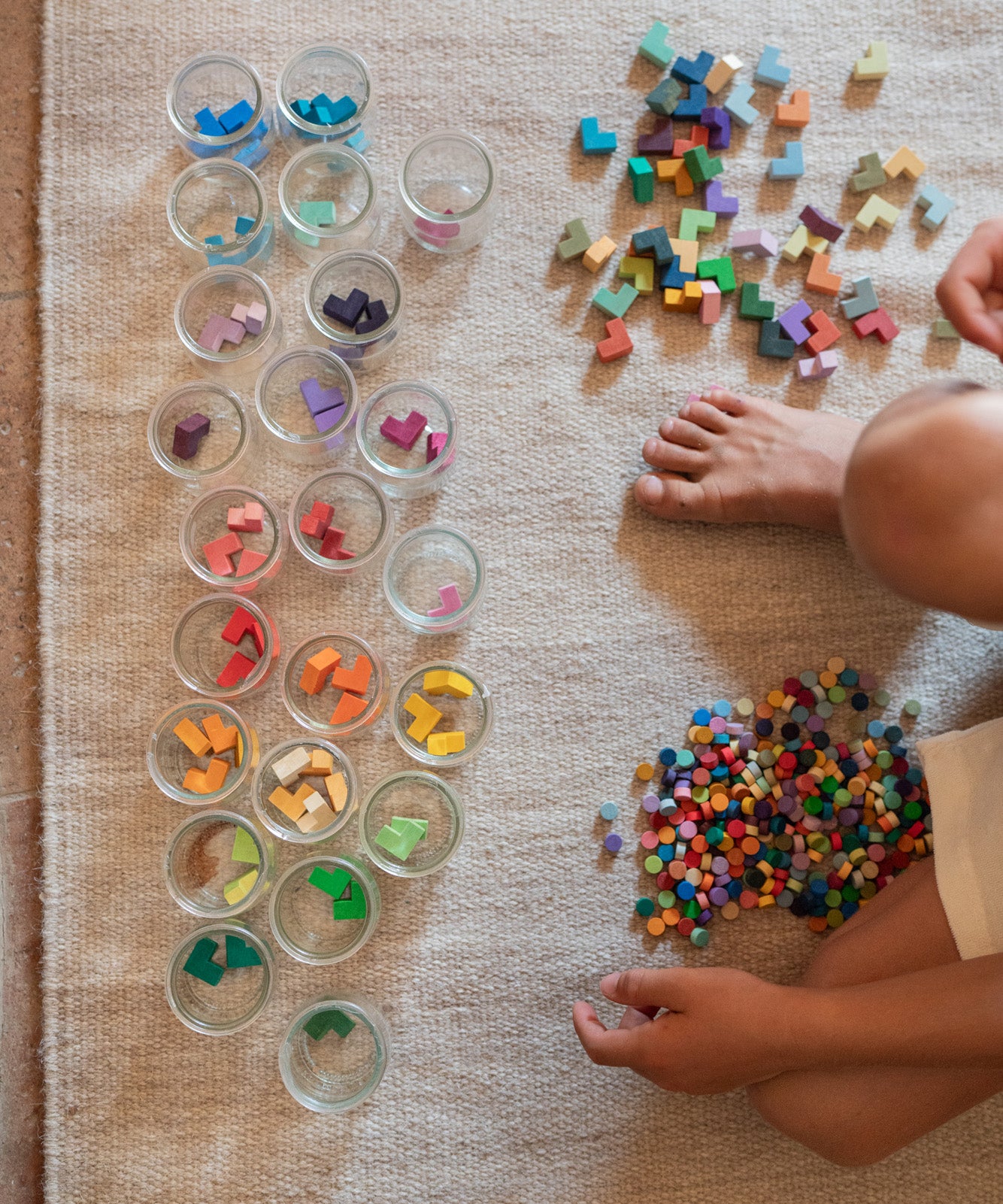 Child playing with the Grapat Mis Match & Bloom set featuring colourful geometric pieces, sorting jars with scattered colourful geometric pieces.