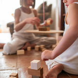 A child playing with the Grapat wooden pendulum set with wooden blocks on the floor, wooden block detail