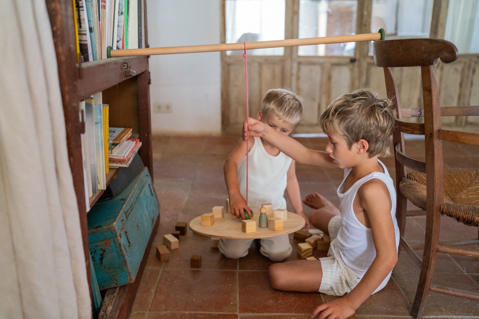 2 children playing with the Grapat wooden pendulum set with wooden blocks on the floor