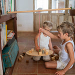 2 children playing with the Grapat wooden pendulum set with wooden blocks on the floor