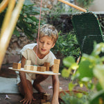 A child playing with the Grapat wooden pendulum set with wooden blocks on the pendulum outside