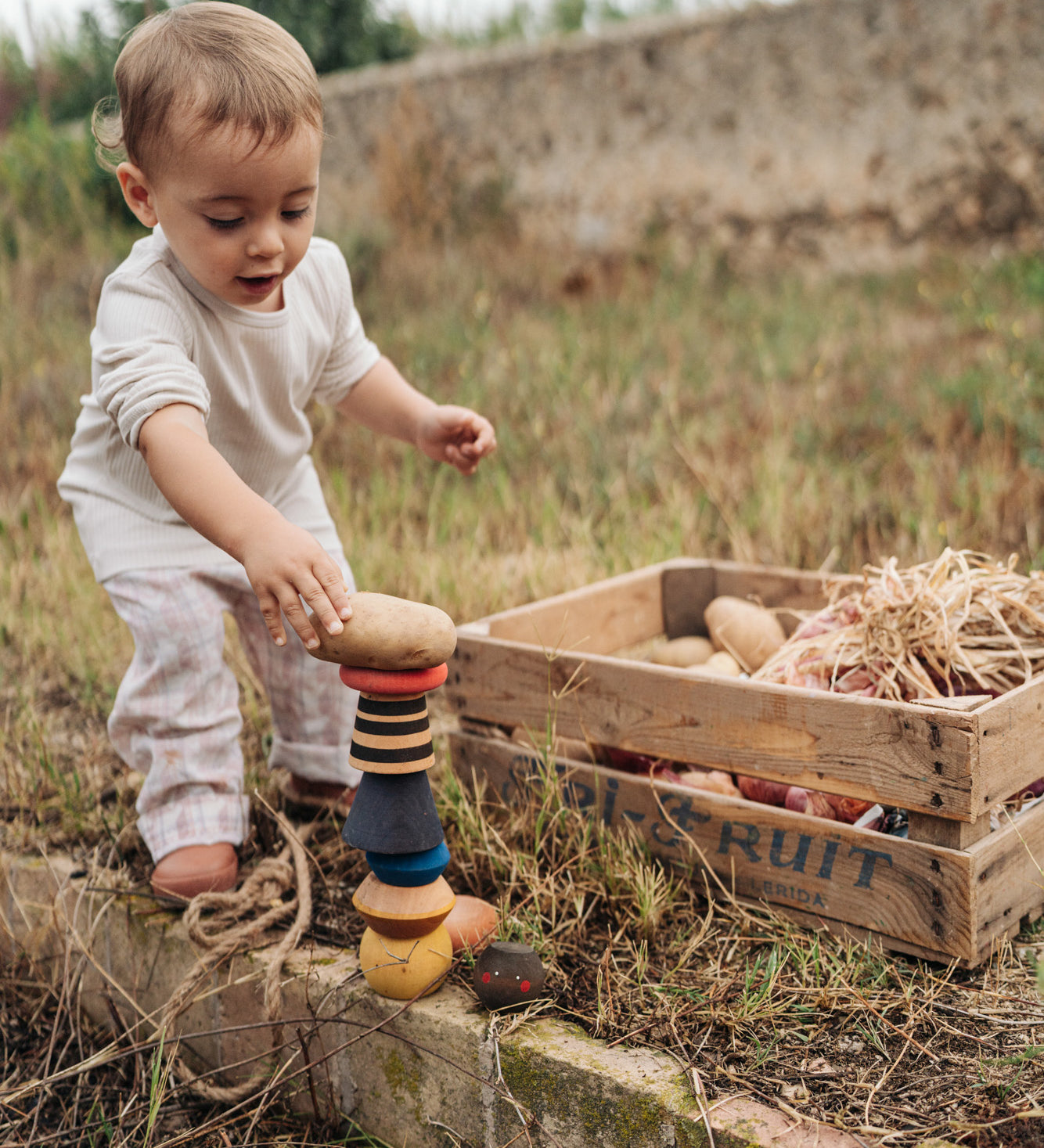 Child playing with the Grapat wooden serendipity stacking set in the garden Showing the different handcrafted tactile pieces stacked on the grass and a potato placed on top of the stack